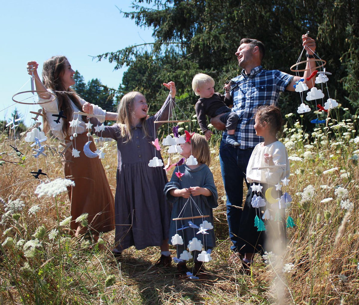 Family holding Sorrel + Fern cloud mobiles in a sunny wildflower meadow