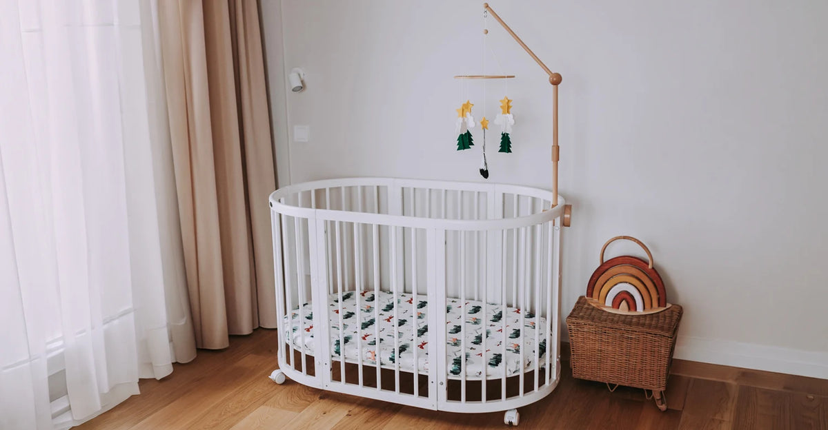 White oval crib with a Starry Woodland mobile and a woven basket in a bright nursery